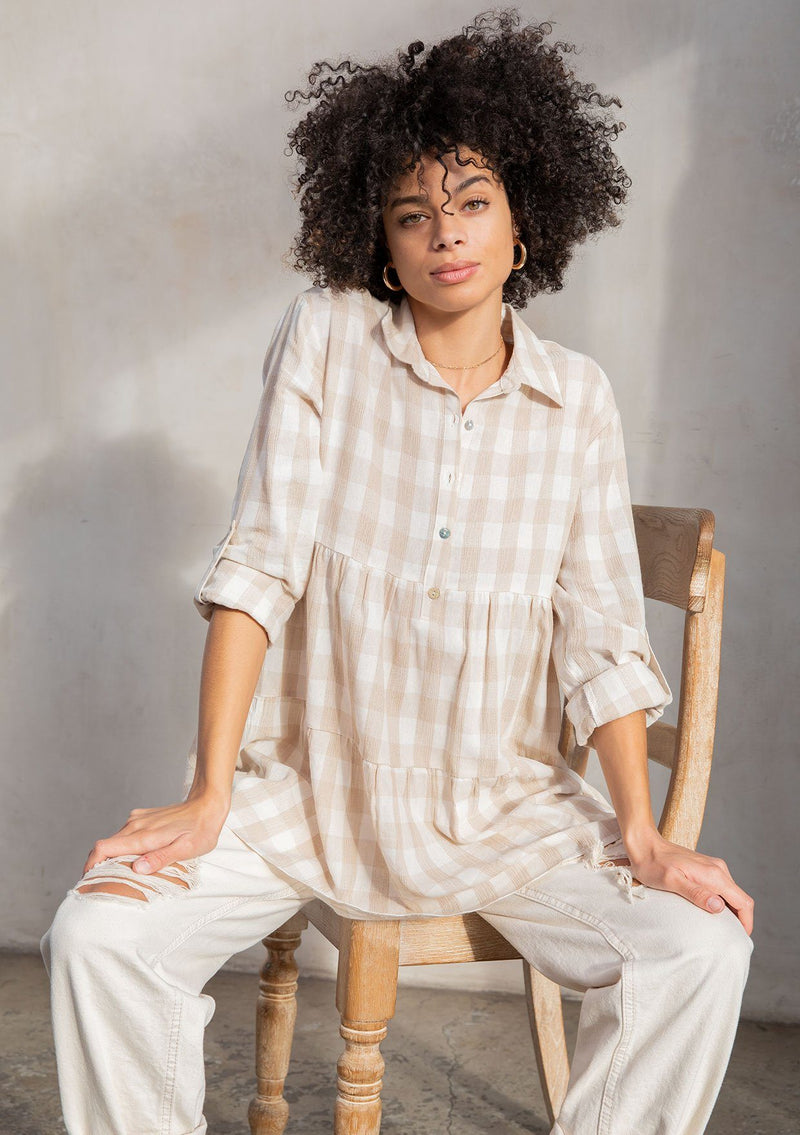 [Color: Taupe/White] A model wearing a relaxed cotton blend beige large gingham button up tunic, with a rolled sleeve, a tiered body, and a long tunic length.