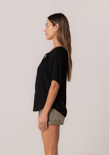 [Color: Black] A side facing image of a brunette model wearing a best selling button front blouse in black. With short puff sleeves, a button front, and a split v neckline with ties.