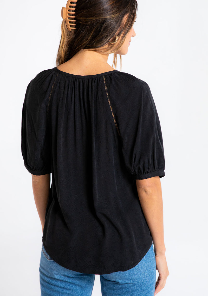 [Color: Black] A model wearing a black puff sleeve button front blouse.