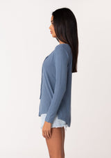 [Color: Denim] A side facing image of a model wearing a blue micro rib long sleeve tee with a v neckline and neck ties. 
