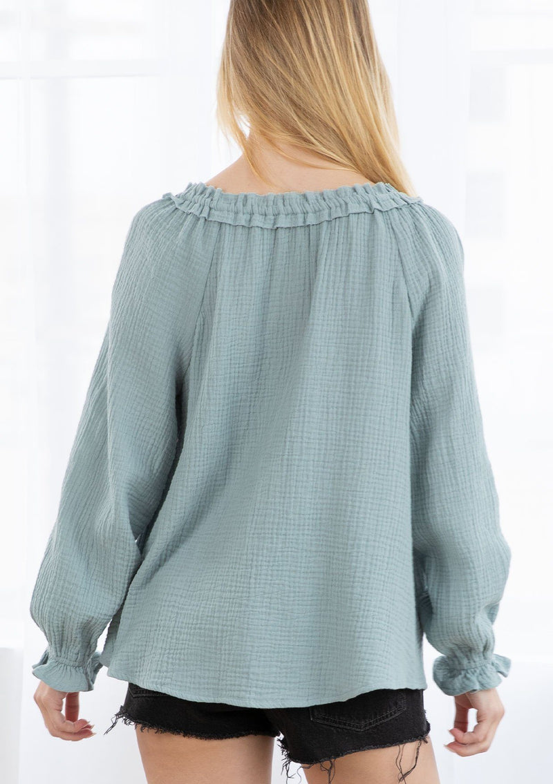 [Color: Dusty Teal] A blond model wearing an airy cotton gauze peasant top. With long voluminous sleeves, a ruffled wrist cuff, and a ruffled split neckline with tassel ties. 