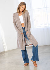 [Color: Natural/Periwinkle] A model wearing a soft knit mid length cardigan with a contrast woven back in a patchwork print. With long sleeves, an open front, and two side patch pockets. 