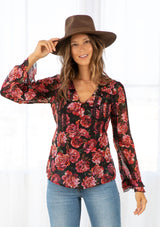 [Color: Black/Magenta] A model wearing a pretty black and red floral print bohemian blouse. A sheer top featuring a metallic clip dot detail throughout, a self covered loop button front, long sleeves with a double flounce cuff, and lace trim throughout. 