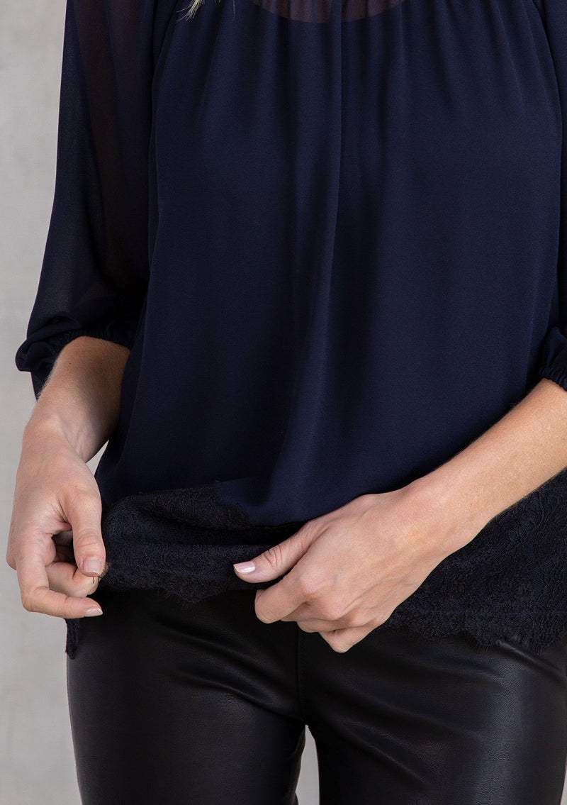[Color: Navy/Black] A model wearing an ethereal sheer navy chiffon blouse with black eyelash lace trim hemline.