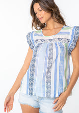 [Color: Blue/Sage] A model wearing a blue and white multi pattern stripe cotton bohemian top with a short ruffled cap sleeve. 