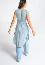 [Color: Blue Fog] A model wearing a floaty blue bohemian sheer cap sleeve tunic top with button front and braided trim. 