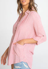 [Color: Red/Ivory] A model wearing a relaxed yarn dye popover tunic shirt in a red and ivory stripe. With long rolled sleeves, a button front, and two patch pocket details.