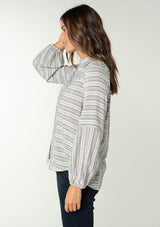 [Color: White/Black] A side facing image of a brunette model wearing a classic bohemian shirt in a white and black stripe. With a button front, long sleeves, and a classic collared neckline. 