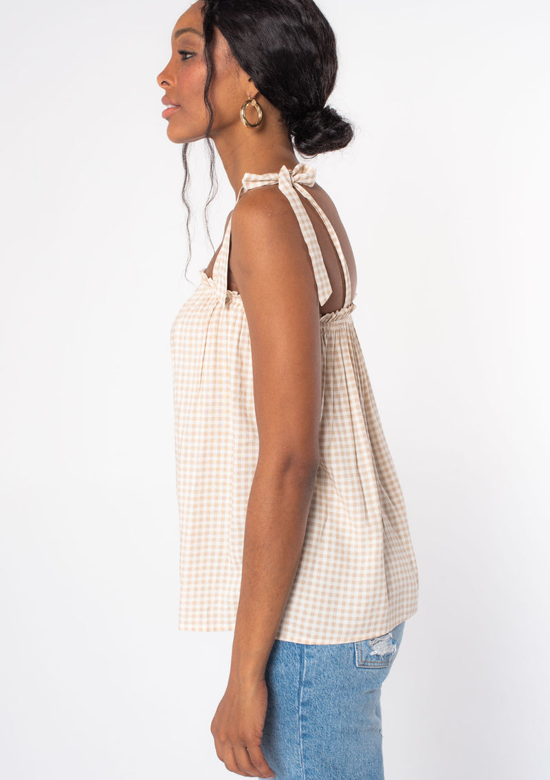 [Color: Tan/Natural] A model wearing a tan and white small checkered gingham print tank top with a tie shoulder detail.