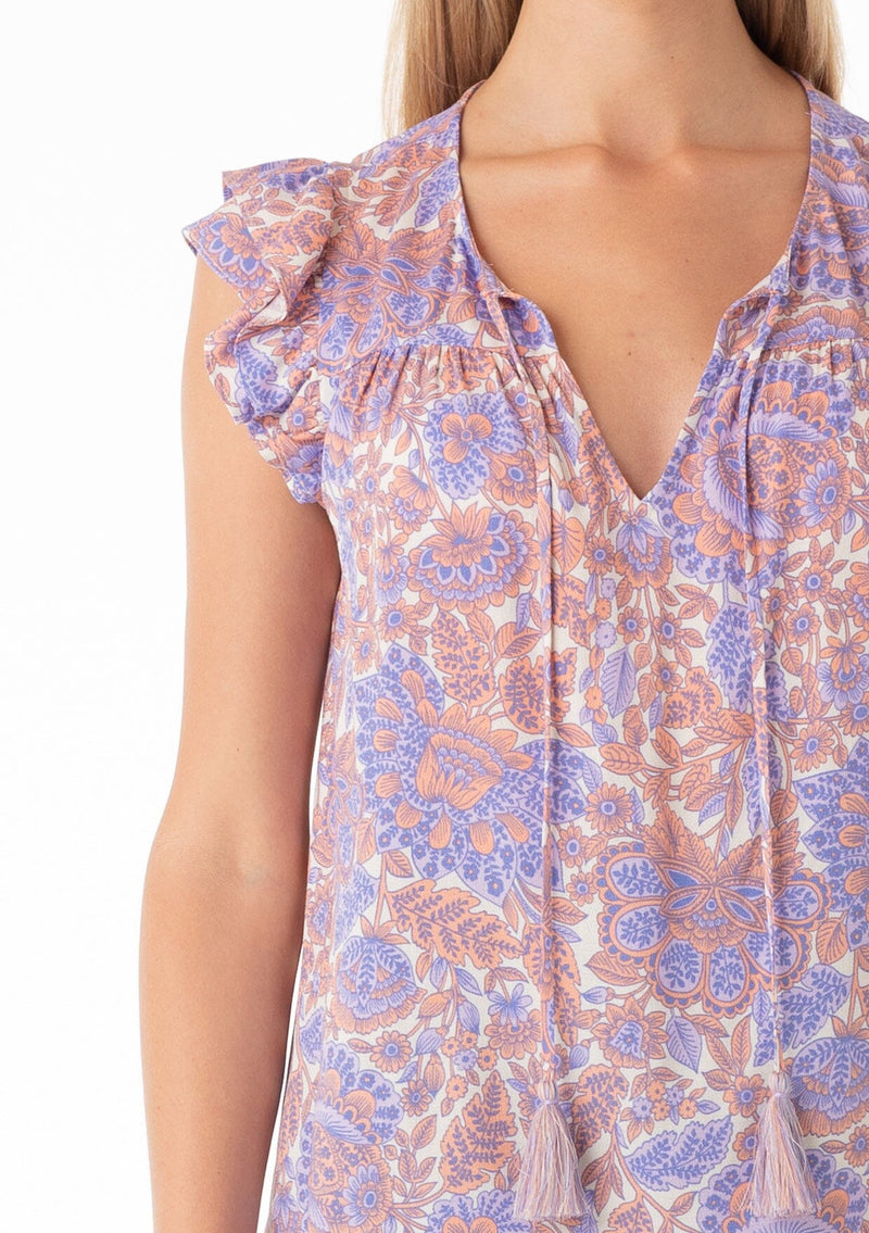 [Color: Ivory/Coral] A close up front facing image of a blonde model wearing a bohemian spring top in a retro inspired purple floral print. With short double flutter cap sleeves, a split v neckline with tassel ties, and a relaxed fit. 