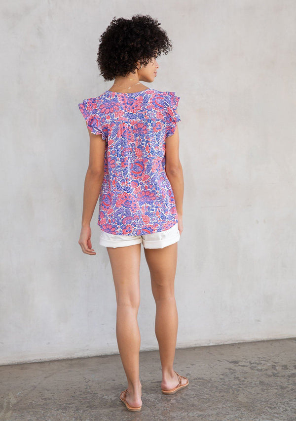 [Color: Ivory/Cobalt] A model wearing a classic bohemian short flutter cap sleeve top in a red and blue paisley print. With a split v neckline and tassel ties. 