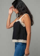 [Color: Black/Natural] A side facing image of a brunette model wearing a black flowy cotton gauze tank top with natural crochet trim and crochet tank top straps.