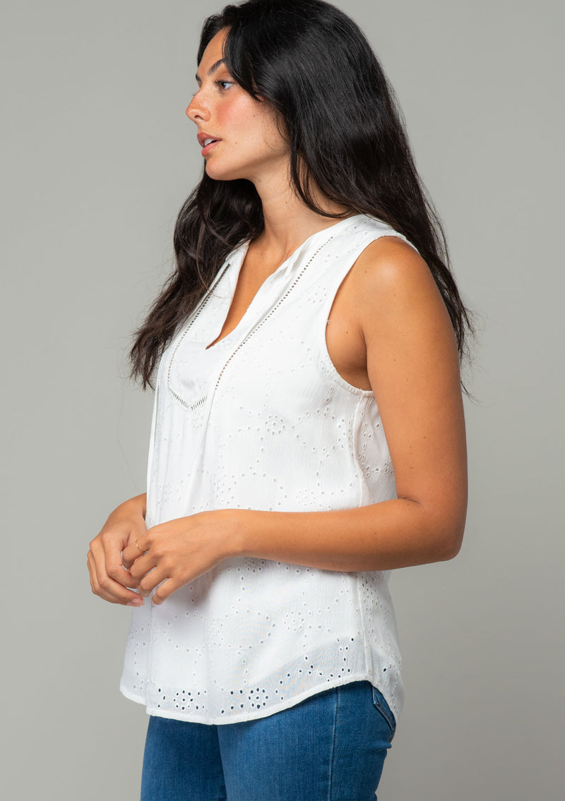[Color: Off White] A side facing image of a brunette model wearing a white eyelet bohemian tank top. With a split v neckline and tassel ties. 