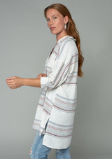 [Color: Ivory/Red] A woman wearing an off white oversized tunic shirt with red striped detail.