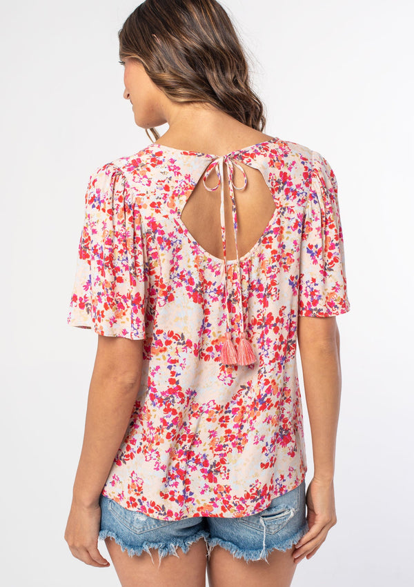 [Color: Blush/Red] A woman wearing a pink and red floral print bohemian top with short flutter sleeves, an open back, and a flowy, relaxed fit. 