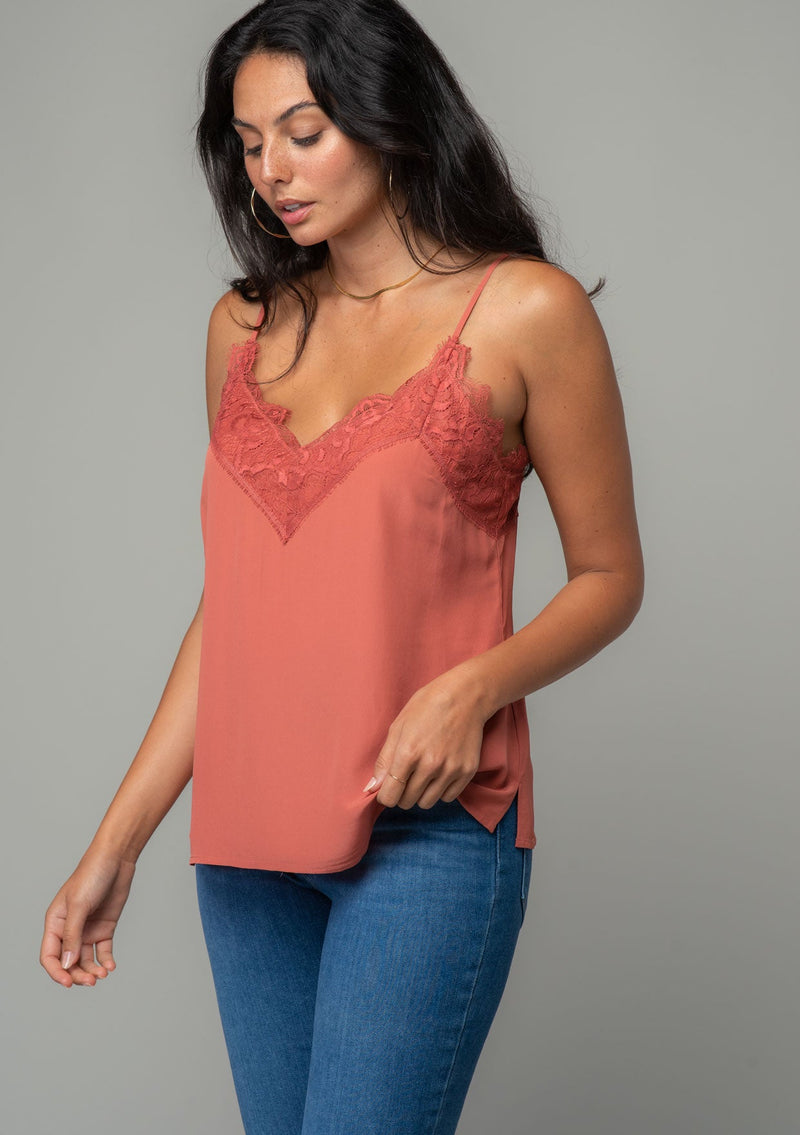 [Color: Rosewood] A front facing image of a brunette model wearing a dusty rose pink lace trim camisole with a v neckline, adjustable spaghetti straps, and a flowy relaxed fit. 