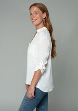 [Color: Gardenia] A half body side facing image of a red headed model wearing a relaxed fit ivory white button front shirt in a lightweight crepe. With long rolled sleeves, a button tab sleeve closure, a front placket, and a collared neckline.