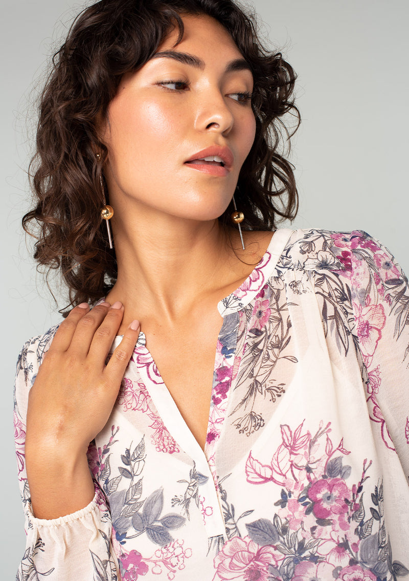 [Color: Natural/Wine] A close up front facing image of a brunette model wearing a sheer chiffon bohemian blouse in a natural and wine purple floral print. With a front placket, long voluminous sleeves, and a flowy relaxed fit. 