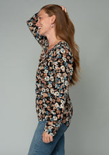 [Color: Black/Natural] A side facing image of a red headed model wearing a lightweight long sleeve top in a black and natural floral print. With a split v neckline and a relaxed flowy fit. 