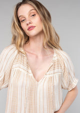 [Color: Natural/Tan] A close up front facing image of a blonde model wearing a bohemian spring top in a natural and tan stripe. With short puff sleeves, a split v neckline with ties, and a flowy relaxed fit. 