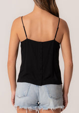 [Color: Black] A back facing image of a brunette model wearing a black bohemian spring camisole tank top with embroidered detail, adjustable spaghetti straps, a scooped neckline, and a self covered button up back detail. The button up back detail on this cute black tank top give it a subtle vintage vibe while the silhouette is modern and flattering.