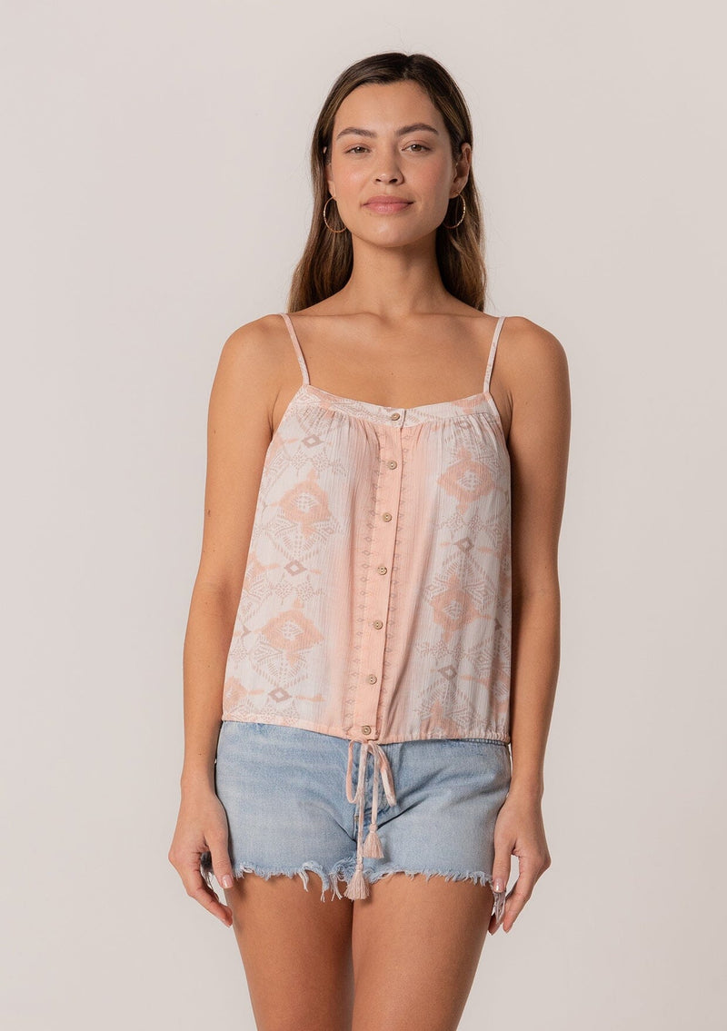 [Color: Natural/Peach] A half body front facing image of a brunette model wearing a summer tank top in a pink bohemian print. With adjustable spaghetti straps, a scoop neckline, a button front, a drawstring waist with tassel ties, and a relaxed fit. 