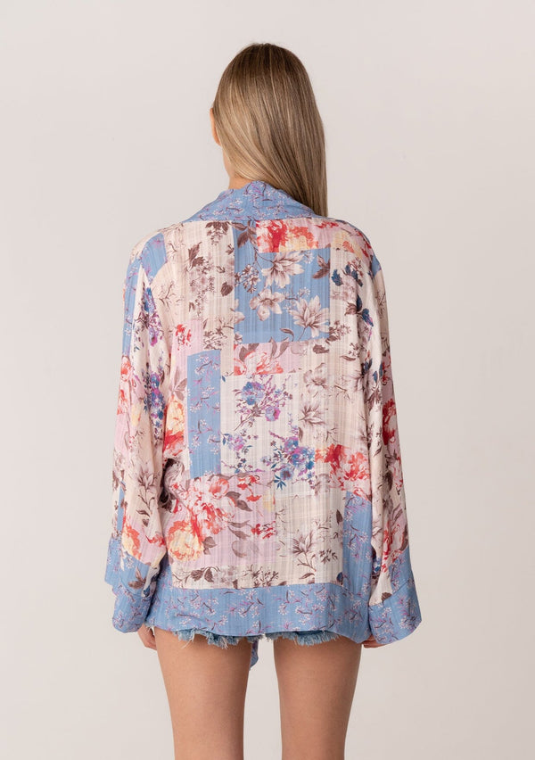 [Color: Natural/Periwinkle] A back facing image of a blonde model wearing a bohemian kimono top in a blue and pink floral print. With long flared sleeves, a relaxed flowy fit, and a tie front waist.