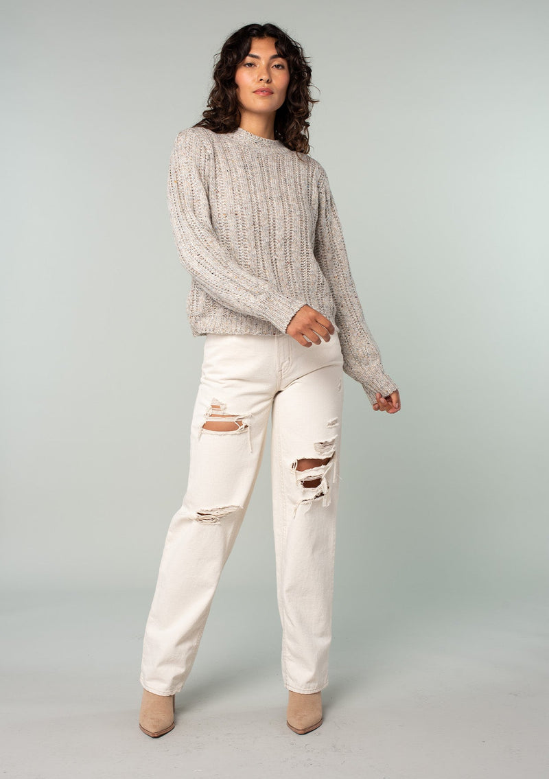 [Color: Oatmeal Multi] A front facing image of a brunette model wearing a perfect vintage style cream colored sweater with modern details. Voluminous long sleeves and a ladder stitch detail add a retro, yet timeless feel to this easy all season layer. Worn here with classic denim. 