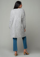 [Color: Heather Grey] A back facing image of a brunette model wearing a heather grey chunky knit cardigan. A fall sweater with long sleeves, cable knit sleeve detail, an open front, and side pockets. 