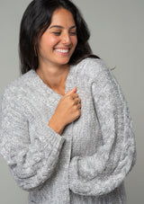 [Color: Heather Grey] A close up front facing image of a brunette model wearing a heather grey chunky knit cardigan. A fall sweater with long sleeves, cable knit sleeve detail, an open front, and side pockets. 