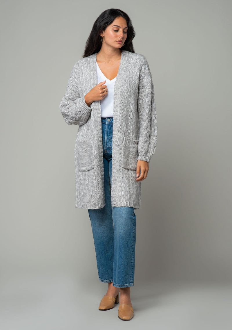 [Color: Heather Grey] A front facing image of a brunette model wearing a heather grey chunky knit cardigan. A fall sweater with long sleeves, cable knit sleeve detail, an open front, and side pockets. 