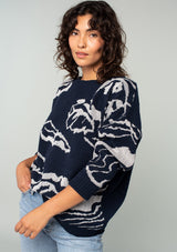 [Color: Navy/Silver] A front facing image of a brunette model wearing a bohemian cotton navy sweater with a silver floral motif. With long sleeves and a crew neckline. 