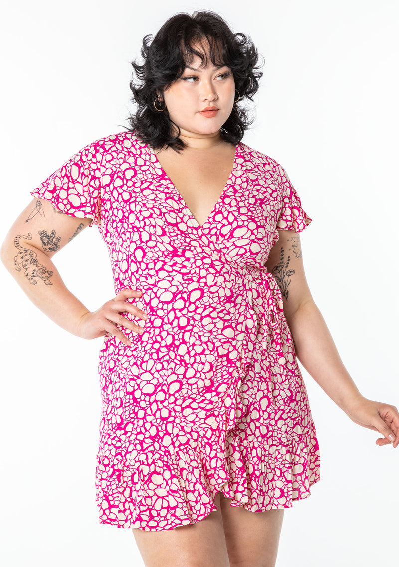 [Color: Natural/Fuchsia] A model wearing a cute and flattering mini wrap dress in a natural and pink abstract circle print. With ruffled hem and flounce sleeve.