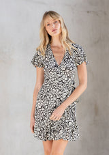 [Color: Natural/Black] A model wearing a cute and flattering mini wrap dress in a natural and black abstract circle print. With ruffled hem and flounce sleeve. 