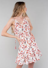[Color: Natural/Rose] A half body front facing image of a blonde model wearing a bohemian spring mini dress in a rose pink floral print. With spaghetti straps, a split v neckline with tassel ties, a smocked elastic waist, and a flowy tiered skirt.