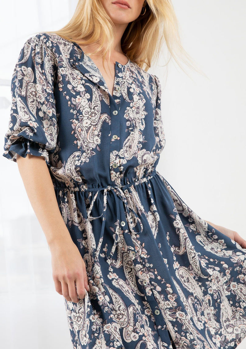 [Color: Denim/Ivory] A blond model wearing a floral print button front mini dress. With half length sleeves, an elastic flounce cuff, and an elastic drawstring waist.