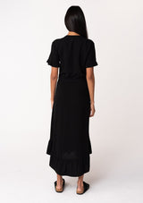 [Color: Black] A back facing image of a model wearing a black mid length shirt dress in a linen blend. Featuring short sleeves with a ruffled trim, a button up front, an adjustable waist tie, and a ruffled hemline.