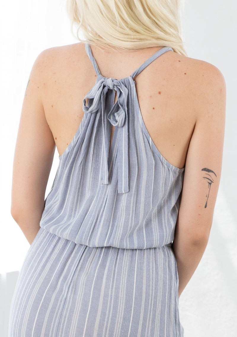 [Color: Chambray/Ivory] A model wearing a chambray blue and ivory striped maxi dress. With a halter neckline, a back tie neck with keyhole detail, an elastic waist, and a tiered skirt. 