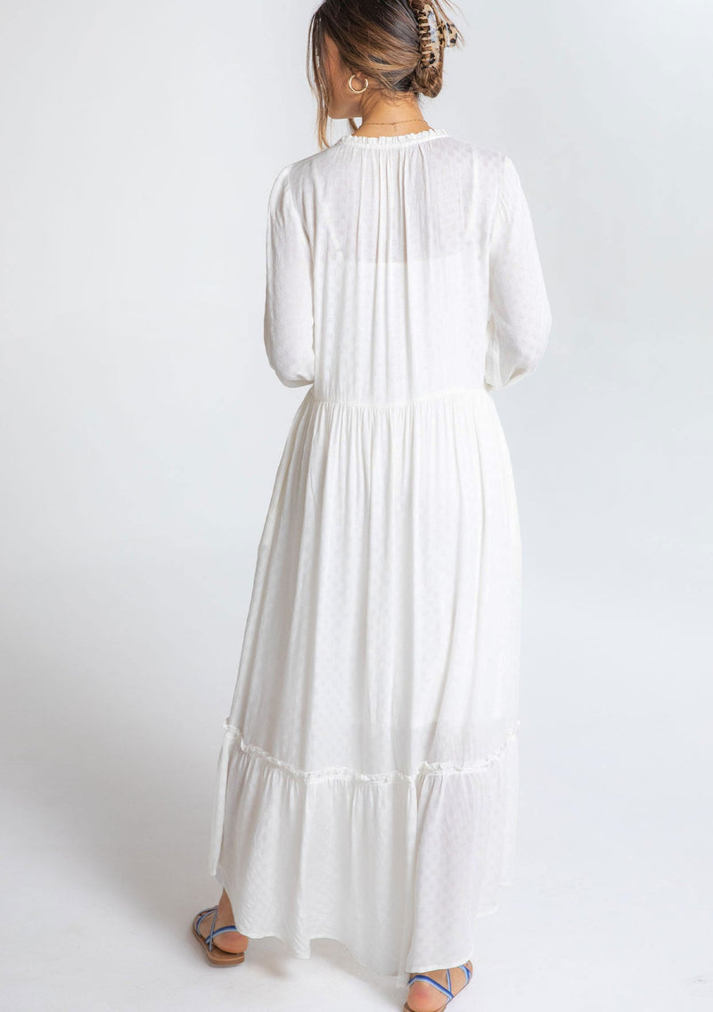 [Color: Chalk] A model wearing a timeless white maxi peasant dress with a button front, ruffled neckline, long voluminous sleeves, and tiered skirt.
