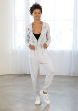 [Color: Heather Grey] A model wearing a heather grey French terry lounge jumpsuit. With long sleeves, an elastic waist, side pockets, a drawstring hoodie, and a front zip. 