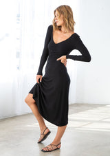 [Color: Black] A model wearing a soft and stretchy black mid length dress in a bamboo micro rib. With a slim fit top, a v neckline, a gathered front detail, long sleeves, and an a line skirt. 