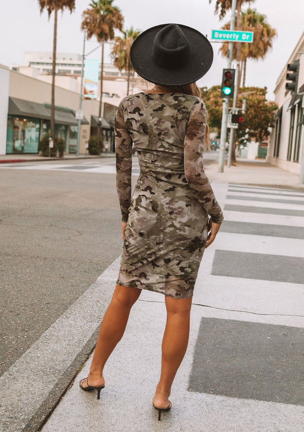 [Color: Olive/Coffee] A model wearing a micro mesh mini dress in a camouflage print. With long sleeves, a round neckline, and a slim bodycon fit.