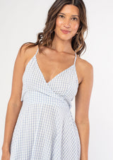 [Color: Periwinkle/White] A woman wearing a cotton blue and white gingham check mid length dress with adjustable spaghetti straps and a tie back detail. 