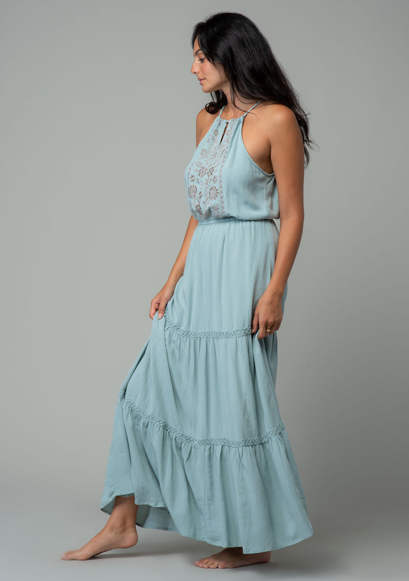 [Color: Seafoam/Taupe] A model wearing a seafoam green flowy bohemian maxi dress with a halter tie neckline and embroidered front.