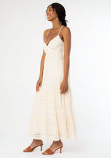 [Color: Natural] A side facing image of a black model wearing a bohemian off white lace maxi dress with spaghetti straps, a flowy skirt, and a v neckline.