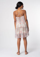 [Color: Blush/Aqua] A model wearing a flowy bohemian mini tank dress in a pink and blue paisley print. A sheer chiffon mini dress with spaghetti straps and a cross strap back detail. 