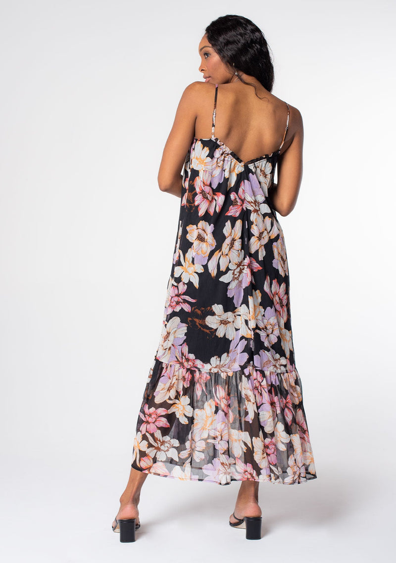 [Color: Black/Lilac] A model wearing a black bohemian maxi tank dress in a purple floral print. A sheer chiffon maxi dress with spaghetti straps and a flowy silhouette. 