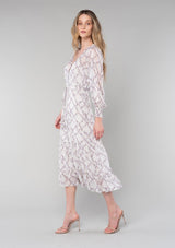 [Color: Ivory/Plum] A side facing image of a blonde model wearing a romantic bohemian mid length chiffon dress in an ivory and plum purple floral print. A spring dress with long sleeves, a self covered button front, a v neckline, a flowy tiered skirt, and a self tie waist belt. 