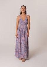 [Color: Dusty Rose/Blue] A front facing image of a brunette model wearing a bohemian summer maxi dress in a pink and blue floral print, with metallic gold clip dot details. Featuring tank top straps, a deep v neckline, a self covered button front, a front slit, a smocked elastic waist, and an open back with strap detail. 