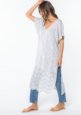 [Color: Lt Heather Grey/Ice] A model wearing a grey and light blue sweater knit tunic top with a long maxi length, side slits, and short sleeves. 